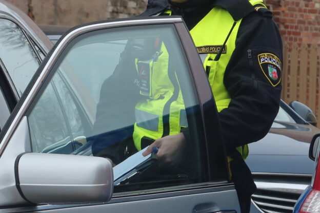 Pašvaldības policijas darbinieks stāv pie atvērtas automašīnas durvīm